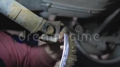 专业的汽车机械金属刷保护生锈的驱动轴部分的汽车在服务站升起。